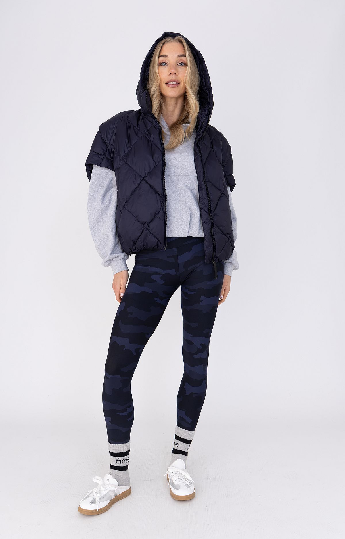 Woman in navy quilted vest over grey hoodie with camo leggings and sneakers