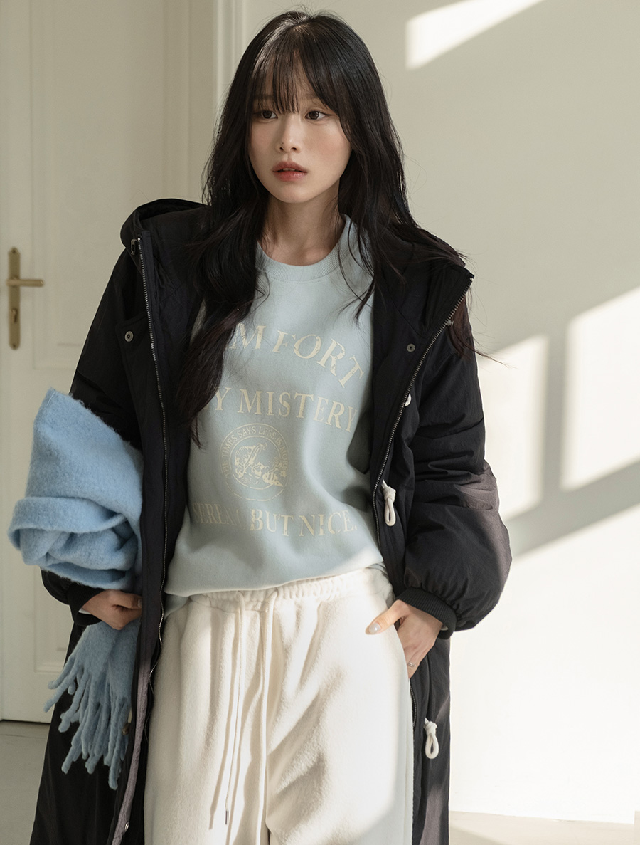 Woman wearing a light blue graphic sweatshirt with cream joggers, a black puffer and a blue scarf