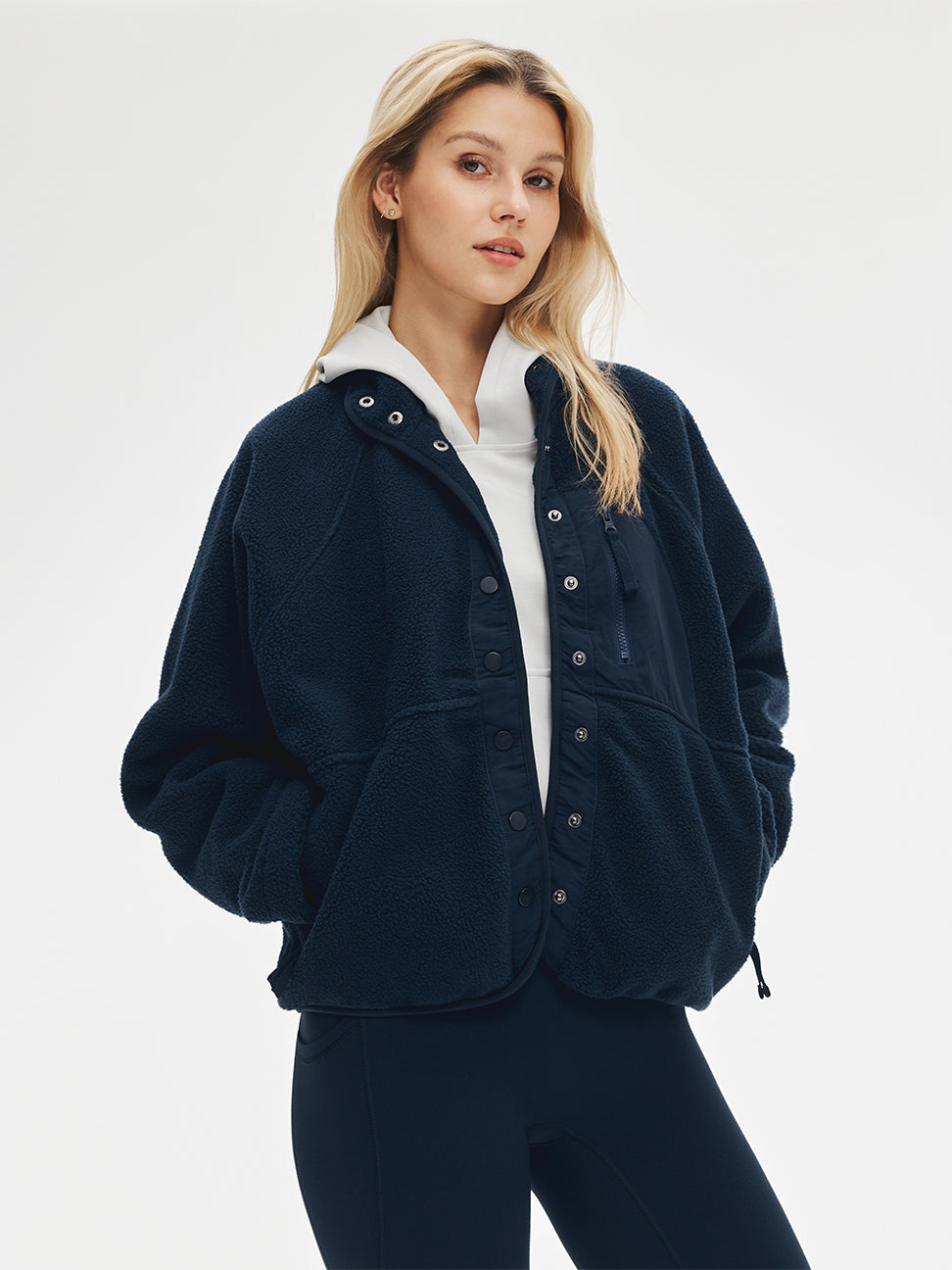 Woman in a navy snap-button fleece jacket over a white hoodie with dark leggings