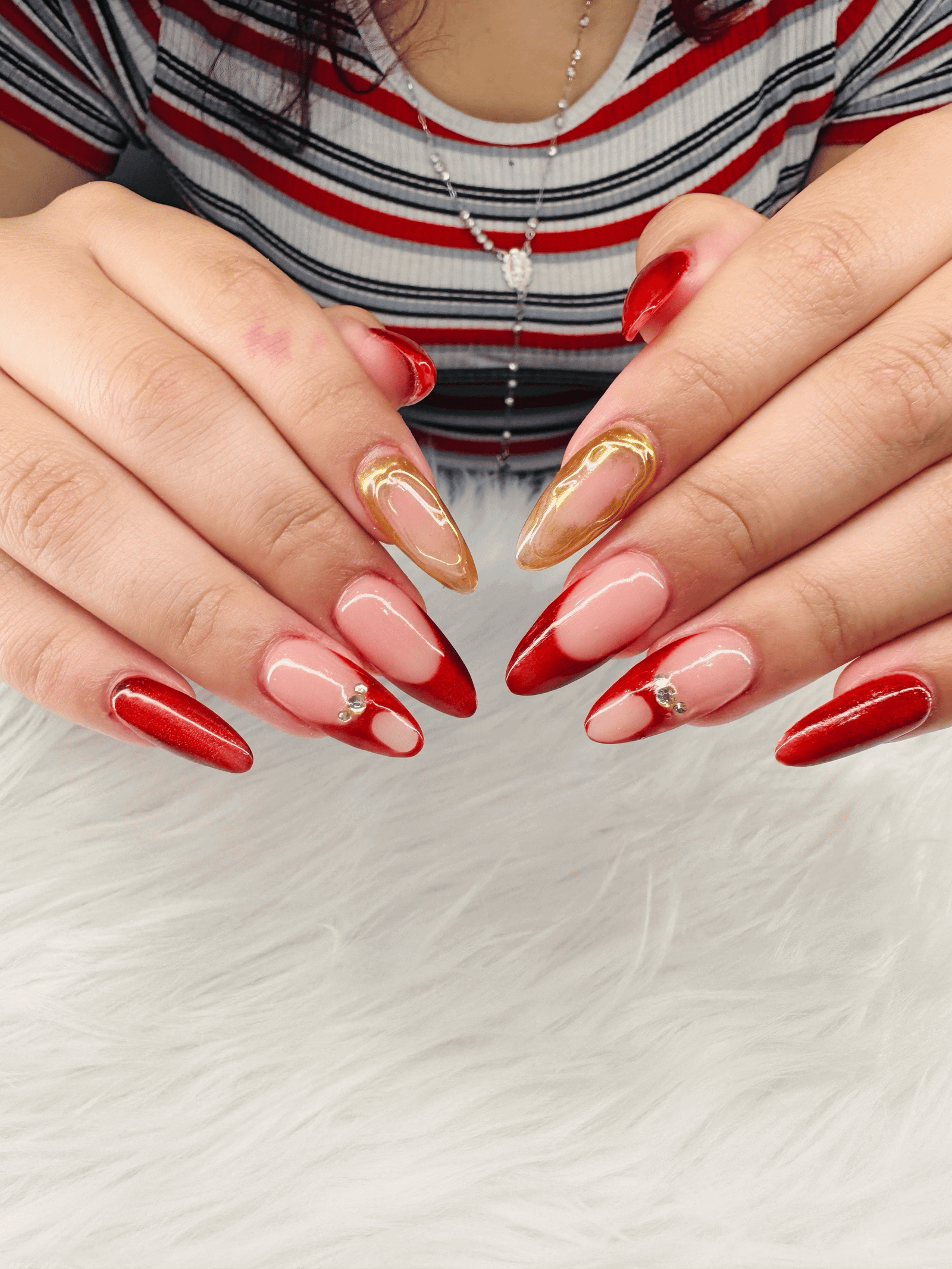Long almond nails with red french tips, gold chrome accents and small crystals