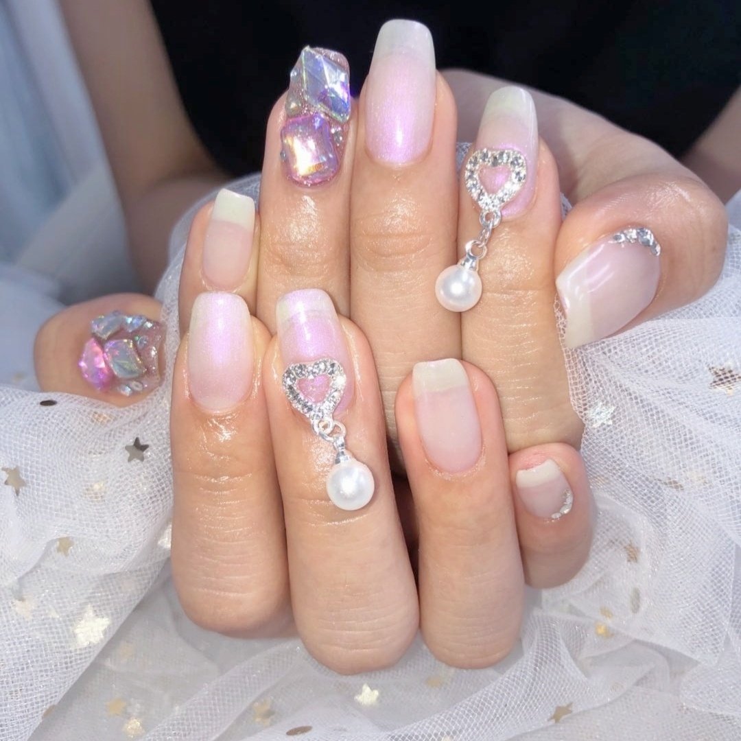Pearly white nails with aurora crystal accents and dangling pearl drop charms in rhinestone heart settings