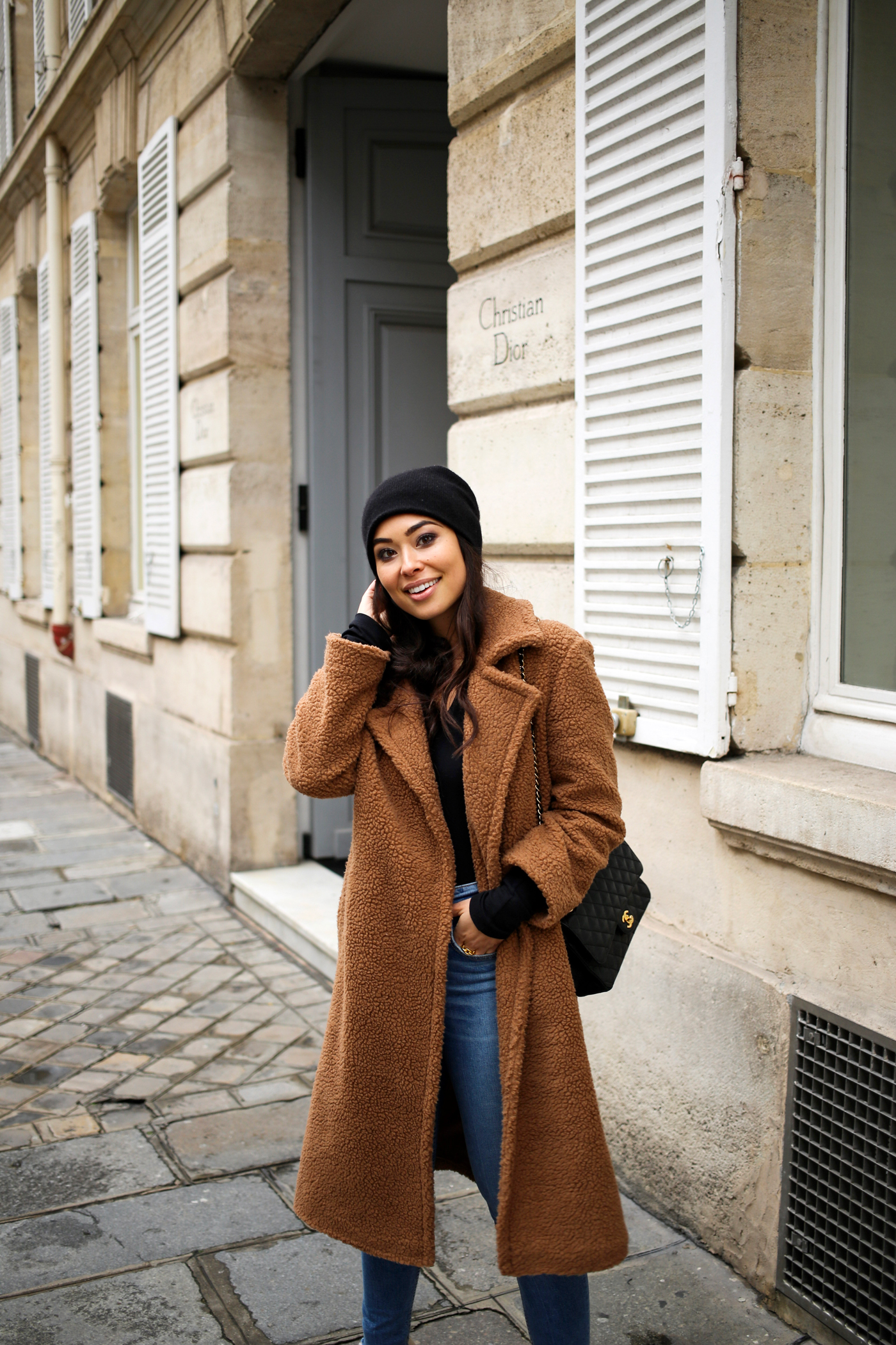 Woman in a long camel teddy coat with skinny jeans and a beanie on a Paris street