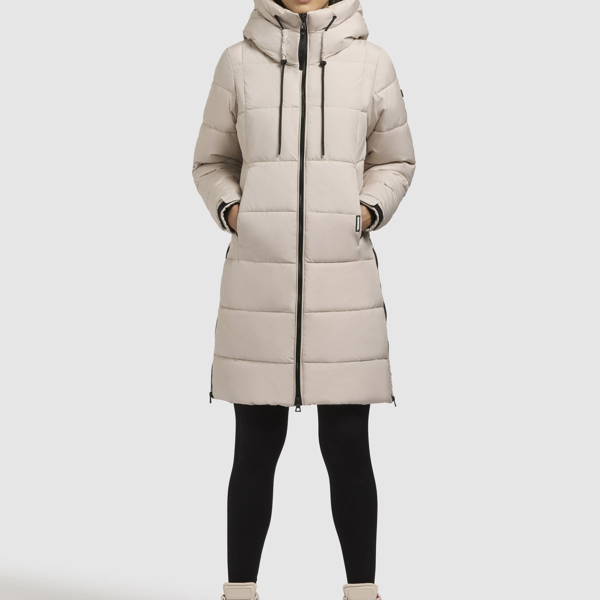 Woman wearing a long beige hooded puffer coat with black leggings and beige boots