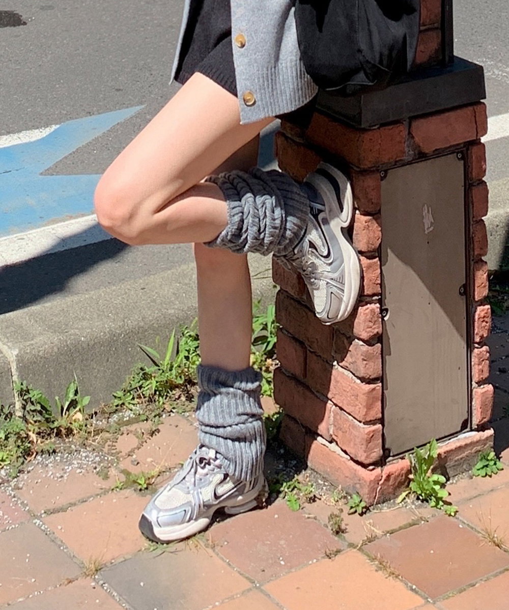 Grey scrunch leg warmers with retro grey sneakers, black knit shorts and a grey cardigan on a city street