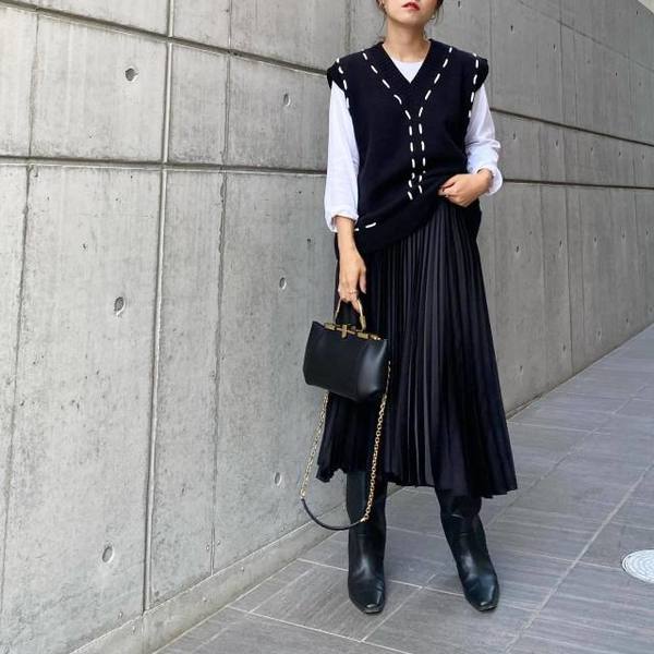 Woman in a knit vest over a white shirt, black pleated midi skirt and black boots