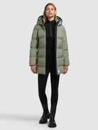 An olive green longline hooded puffer worn over a black top, black leggings and black lace-up boots.