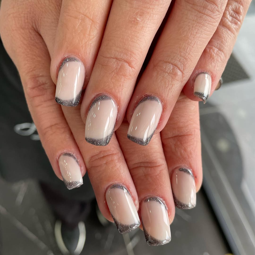 Short squoval nails with sheer nude base and dark gray silver-glitter French tips