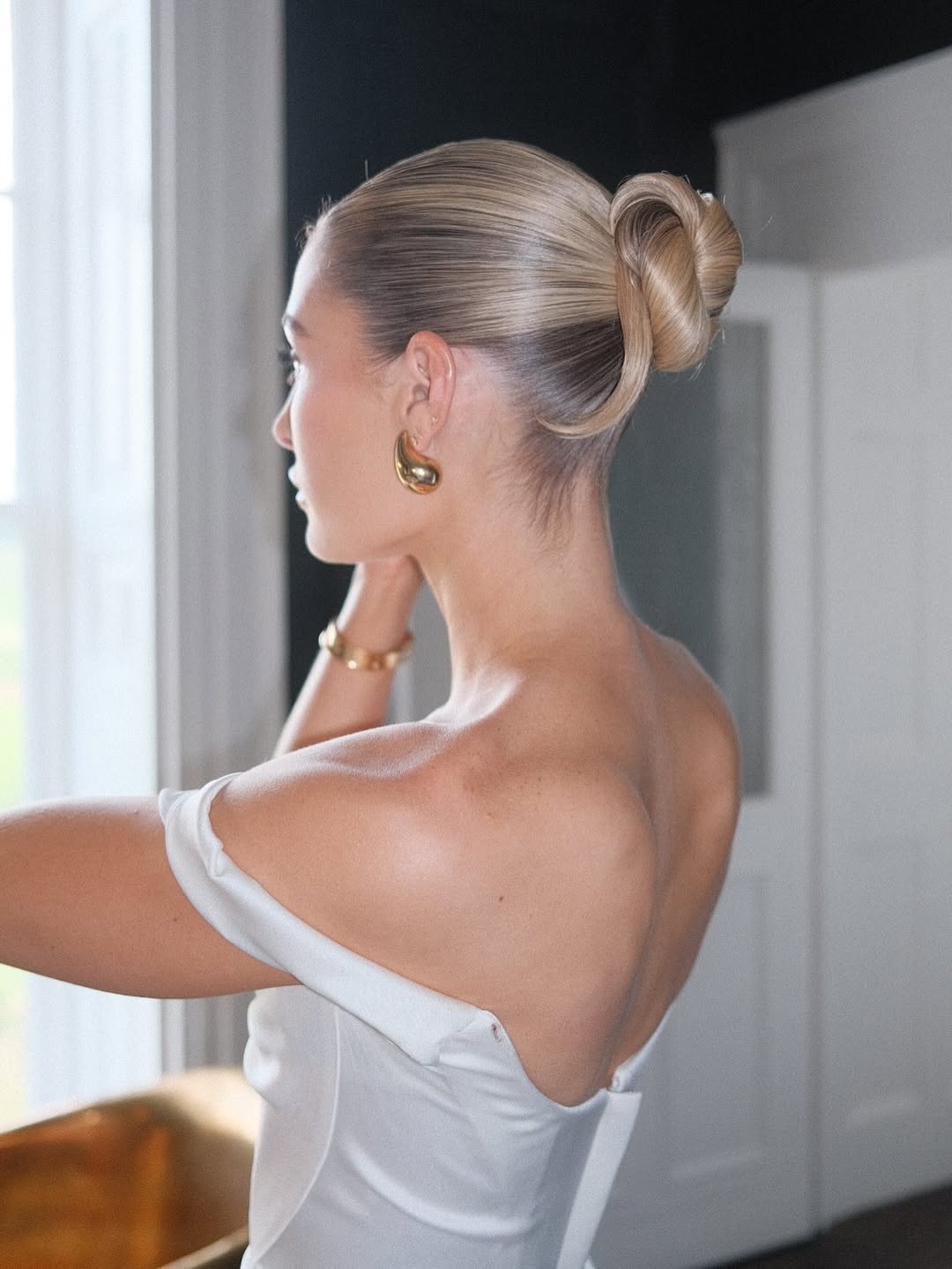 Sleek high bridal bun with large gold statement earrings