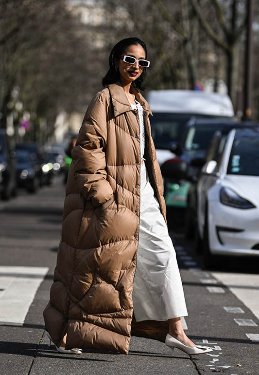 A woman wearing a long camel puffer coat with a ribbed knit dress