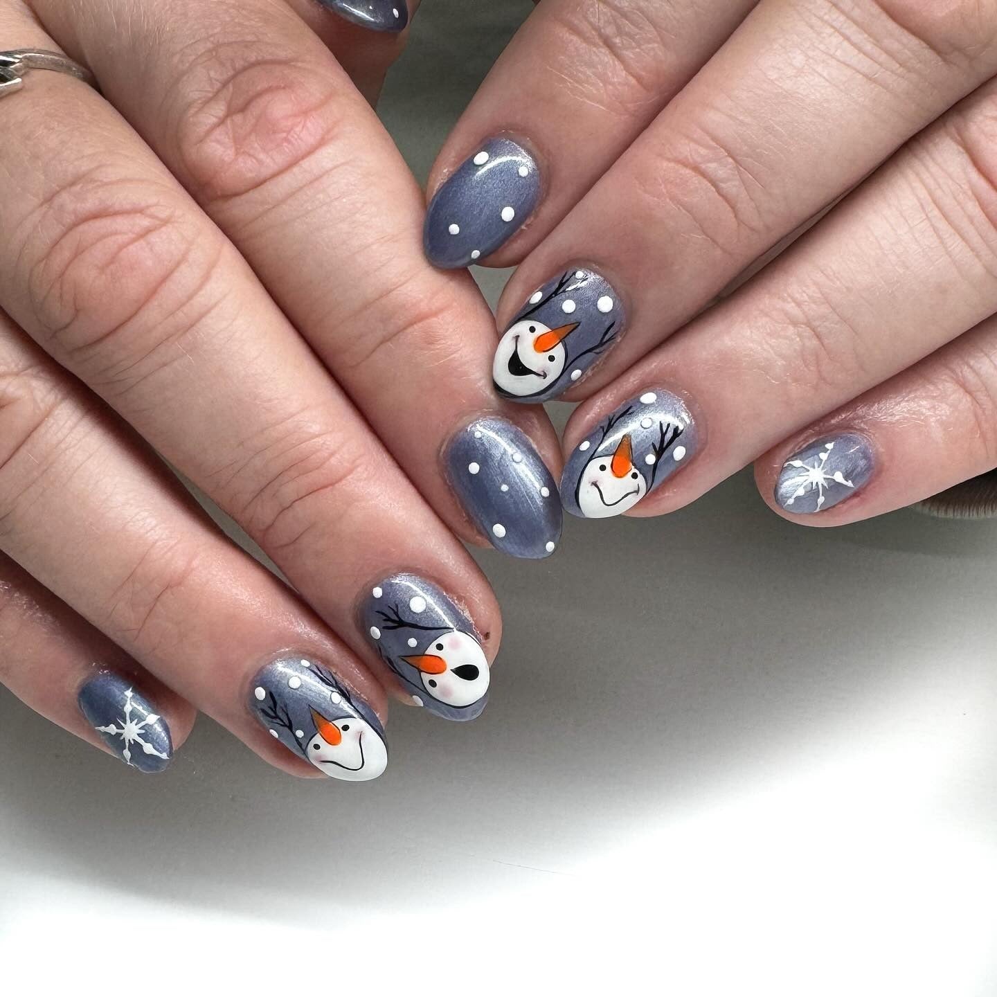 Steel-blue nails with hand-painted snowman faces, snow dots, and snowflakes.