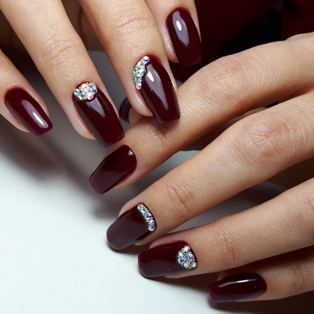 Glossy deep wine oval nails with a curved line of rhinestones tracing each cuticle