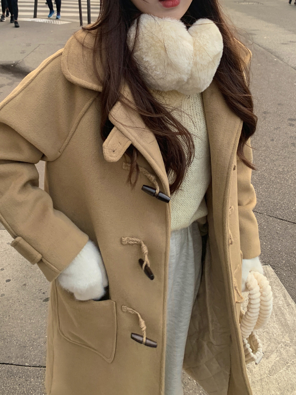 Close-up of a camel toggle duffle coat with wooden toggles over a cream knit sweater with faux-fur earmuffs and white gloves