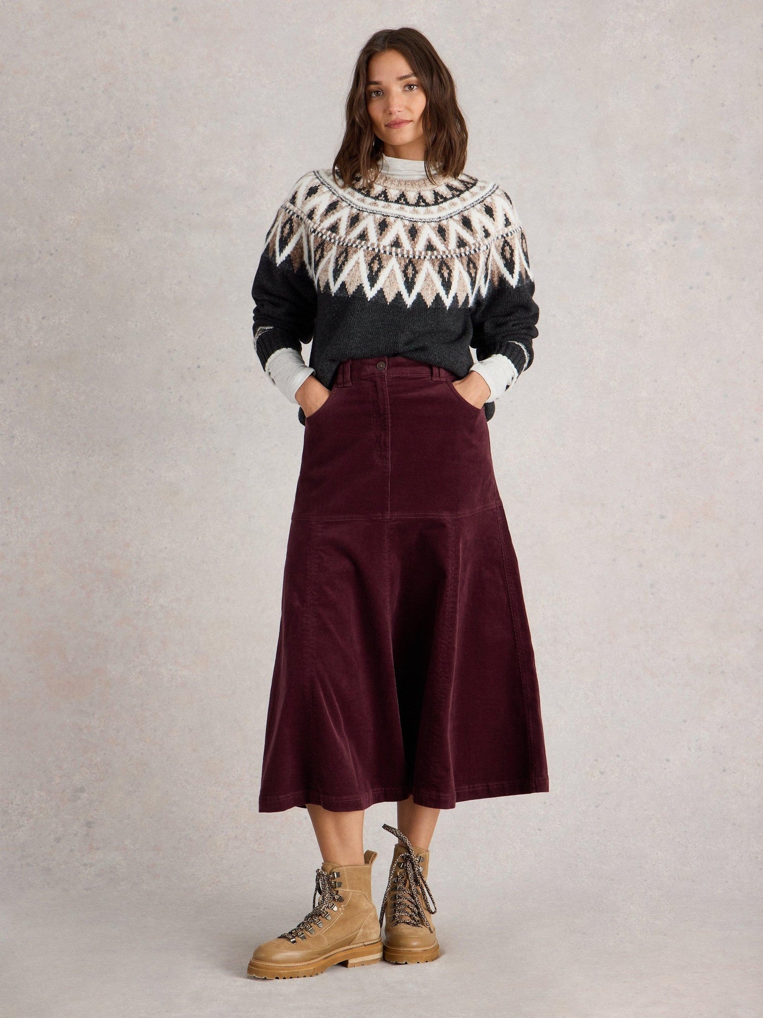 Woman in a black Fair Isle yoke sweater with a burgundy corduroy midi skirt and tan hiking boots