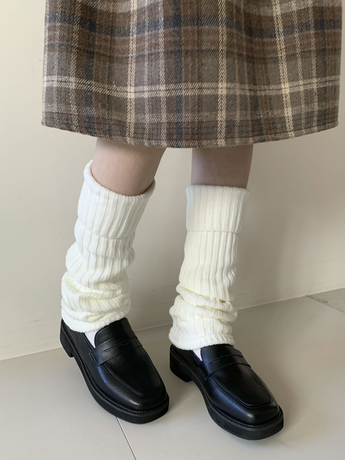 Chunky white ribbed leg warmers with a brown plaid pleated skirt and black loafers