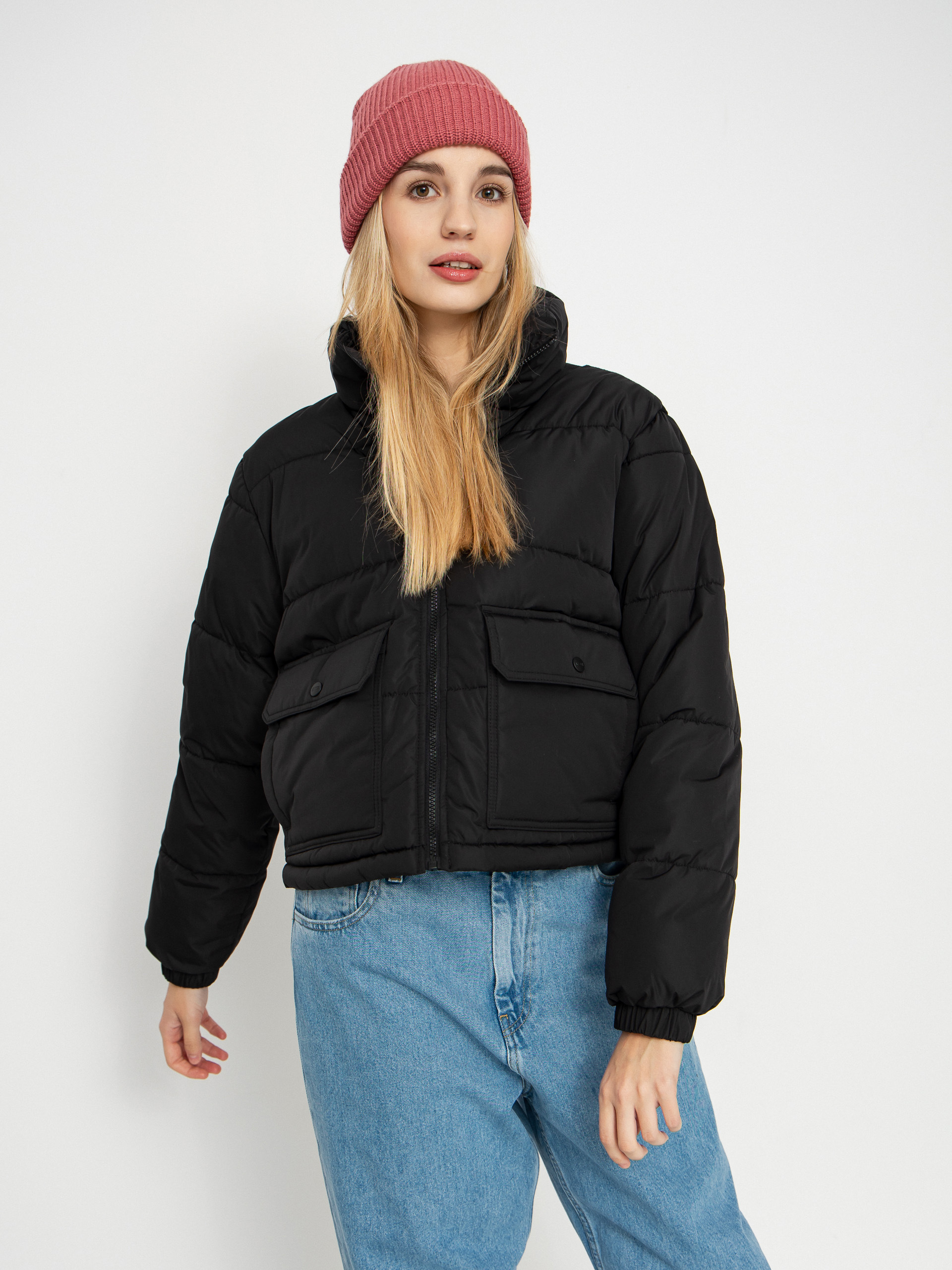 Woman in a black cropped puffer jacket, light-wash jeans and a pink beanie