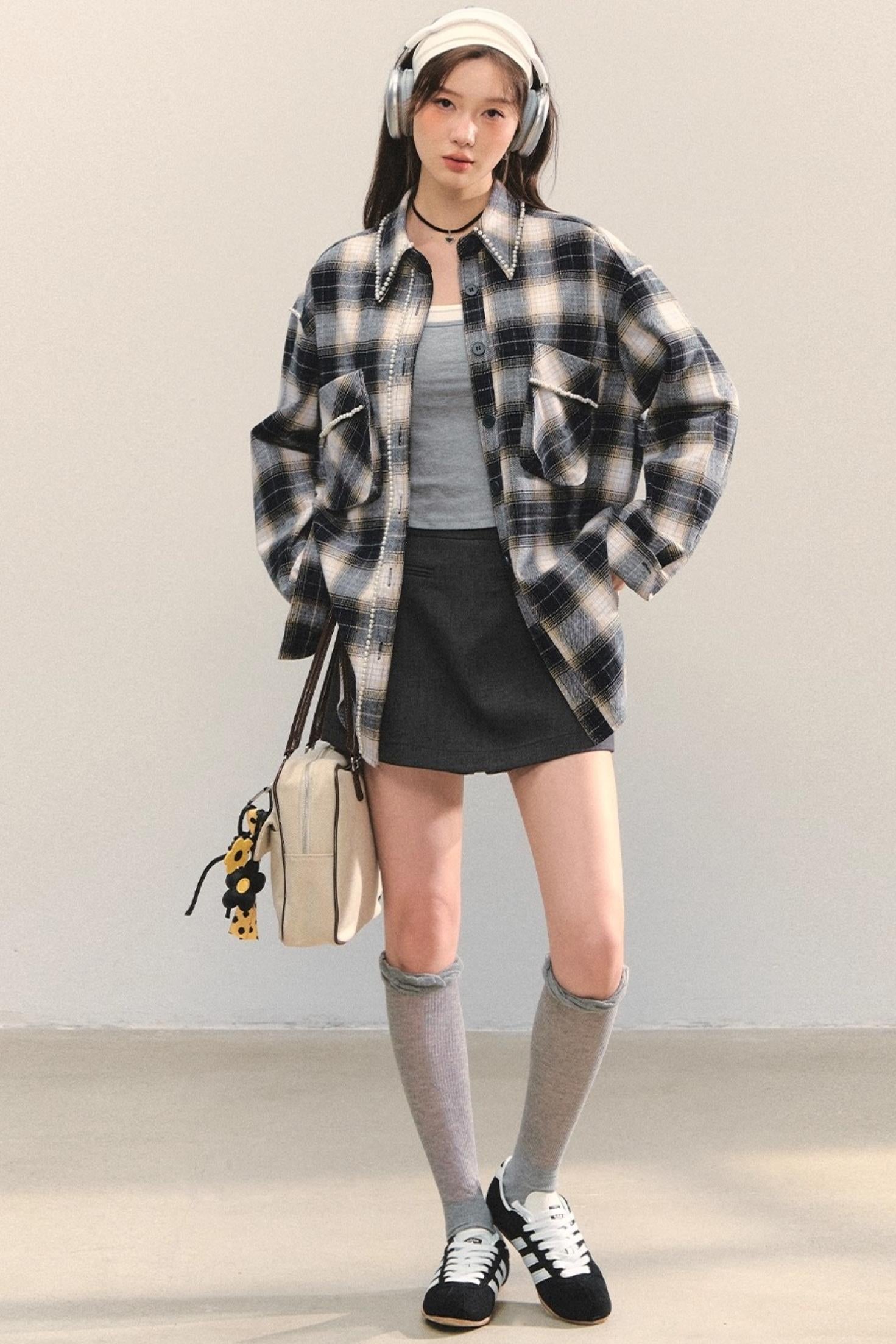 Woman in an oversized black-and-white plaid flannel shirt over a gray tank with a black mini skirt, gray knee-high socks, and black sneakers, wearing a headband and headphones