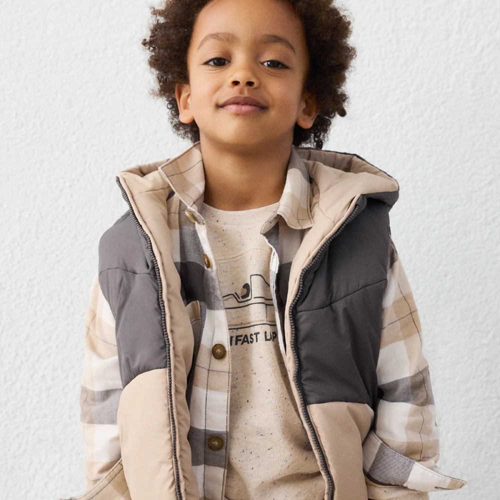 A boy's reversible quilted vest layered over a plaid flannel shirt