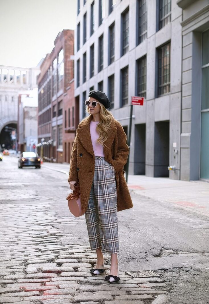 Woman in a camel teddy coat with a pink top, plaid cropped trousers, beret and bow flats