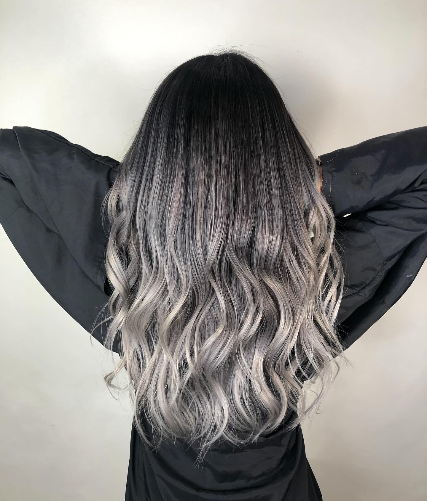 Back view of long wavy hair with near-black roots melting into silver-ash grey ends