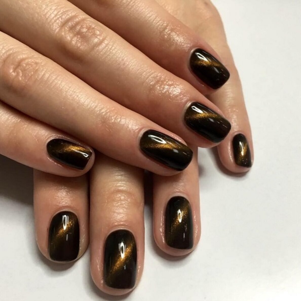Short oval dark chocolate nails with a golden shimmer streak across each nail