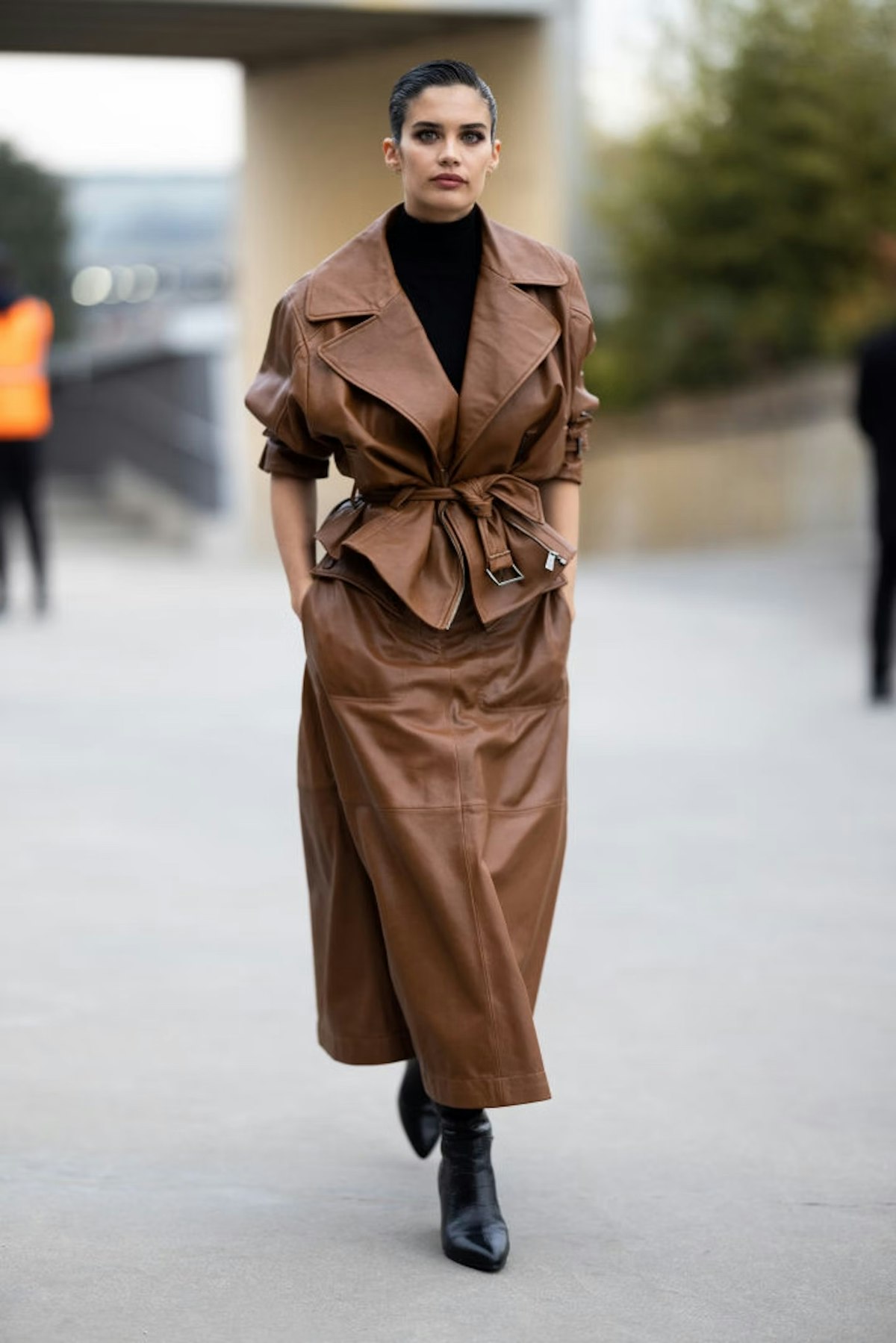 Woman in brown leather trench coat with brown leather maxi skirt and black boots