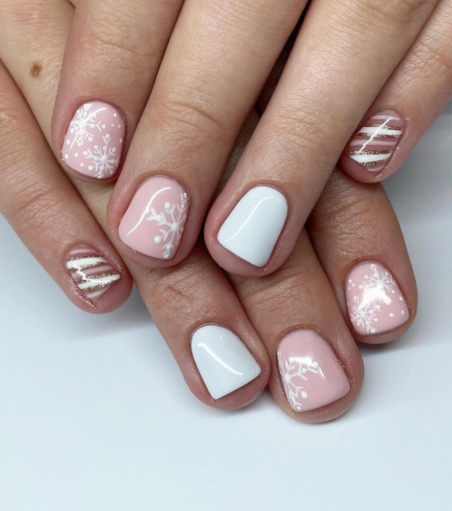 Short blush pink Christmas nails with white snowflakes, white accents and gold striped swirls