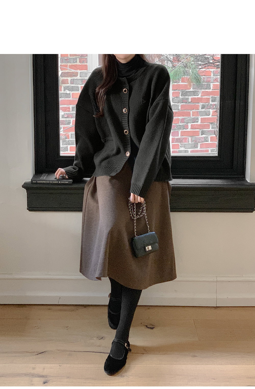 Woman wearing a black knit cardigan over a black turtleneck with a brown midi skirt and black tights