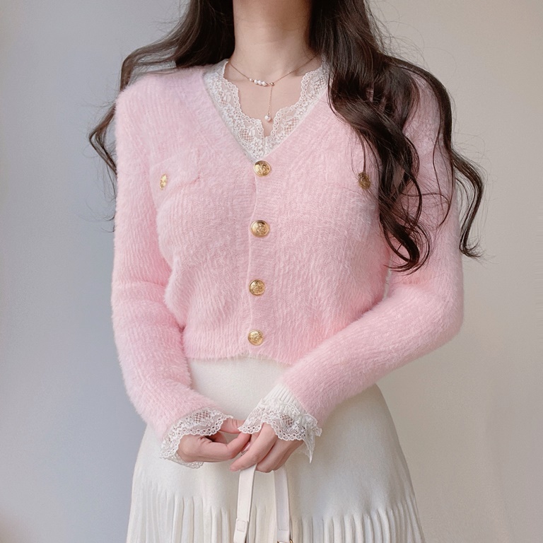 Close-up of a pink fuzzy cardigan with gold buttons worn over a white lace-trimmed top and pleated skirt