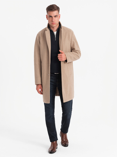 Man wearing a beige single-breasted topcoat over a black knit with dark jeans and chelsea boots