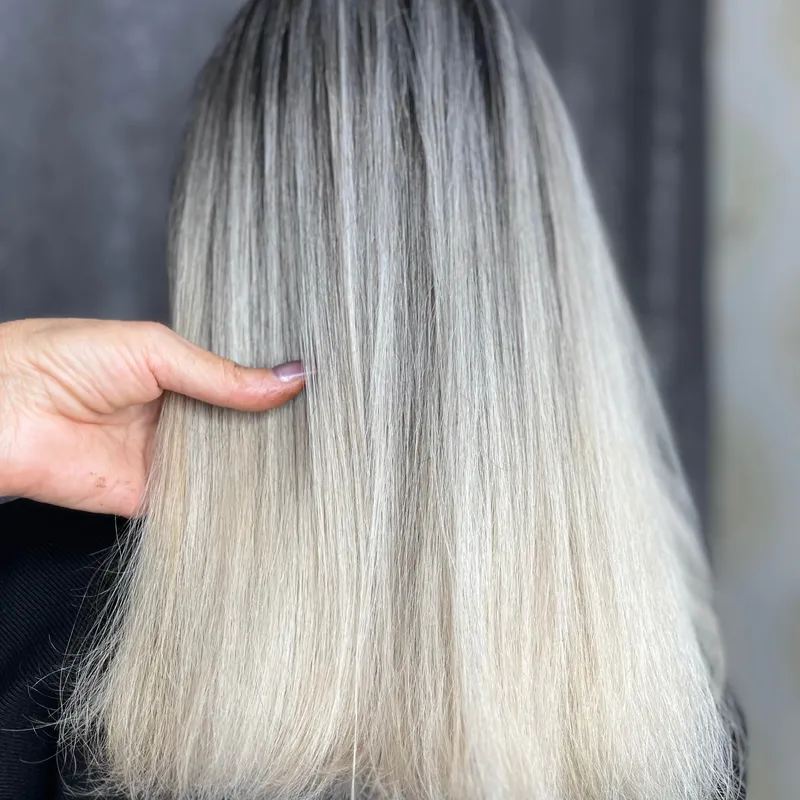 Ash blonde balayage on long hair with dark shadow root, salon back view