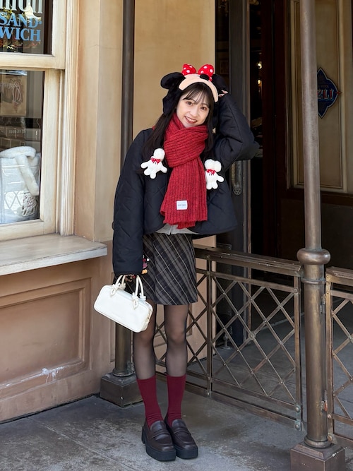 Woman at a theme park wearing a mouse-ear headband, red scarf, black puffer jacket and plaid mini skirt