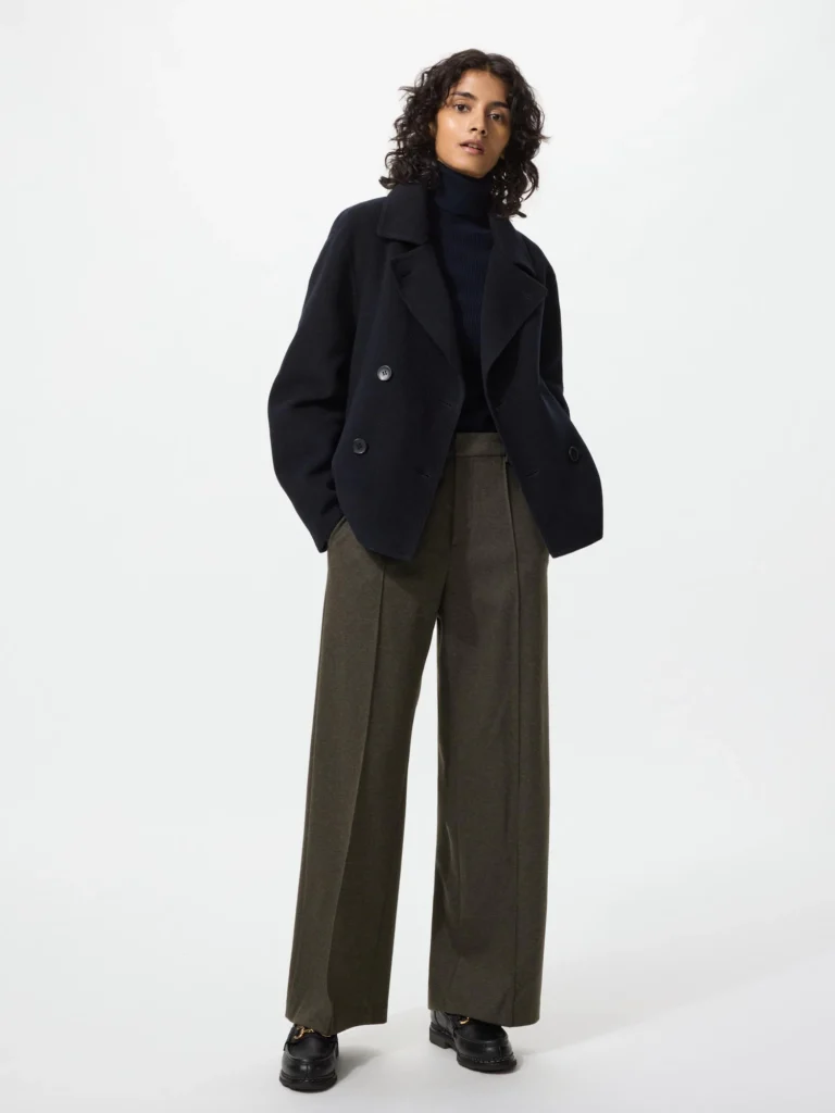 Model in a black double-breasted pea coat with dark wide-leg wool trousers and black loafers