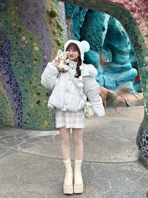 Woman at a theme park in a white puffer jacket, mini skirt, cream boots and mouse-ear headband holding a plush toy
