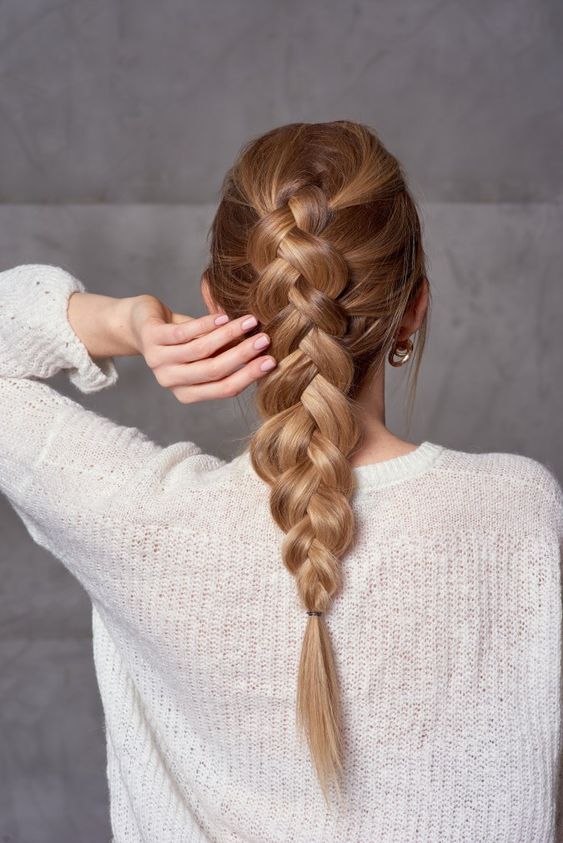 Back view of a woman with long honey-blonde hair in a classic Dutch braid, wearing a white knit sweater