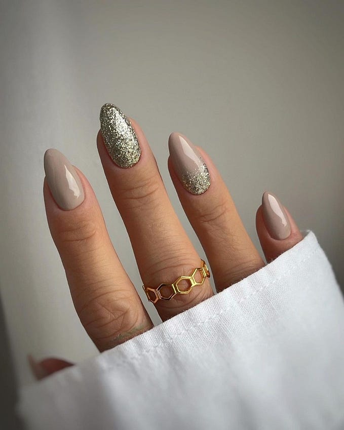 Taupe-nude nails with one full gold glitter accent nail and a glitter fade