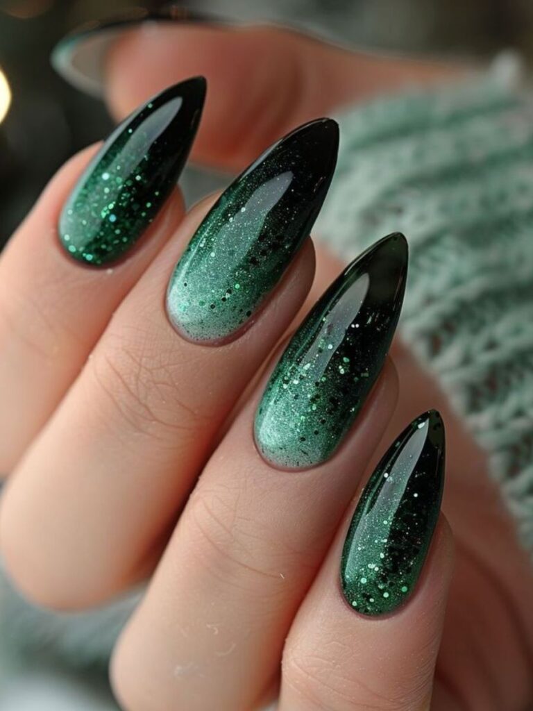 Long stiletto-almond nails fading from deep emerald green at the base to black tips with subtle glitter