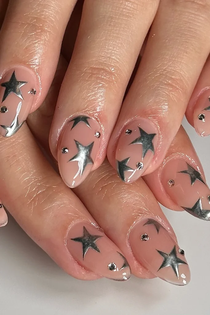 Almond nails with sheer nude base decorated with large silver chrome stars and small rhinestones
