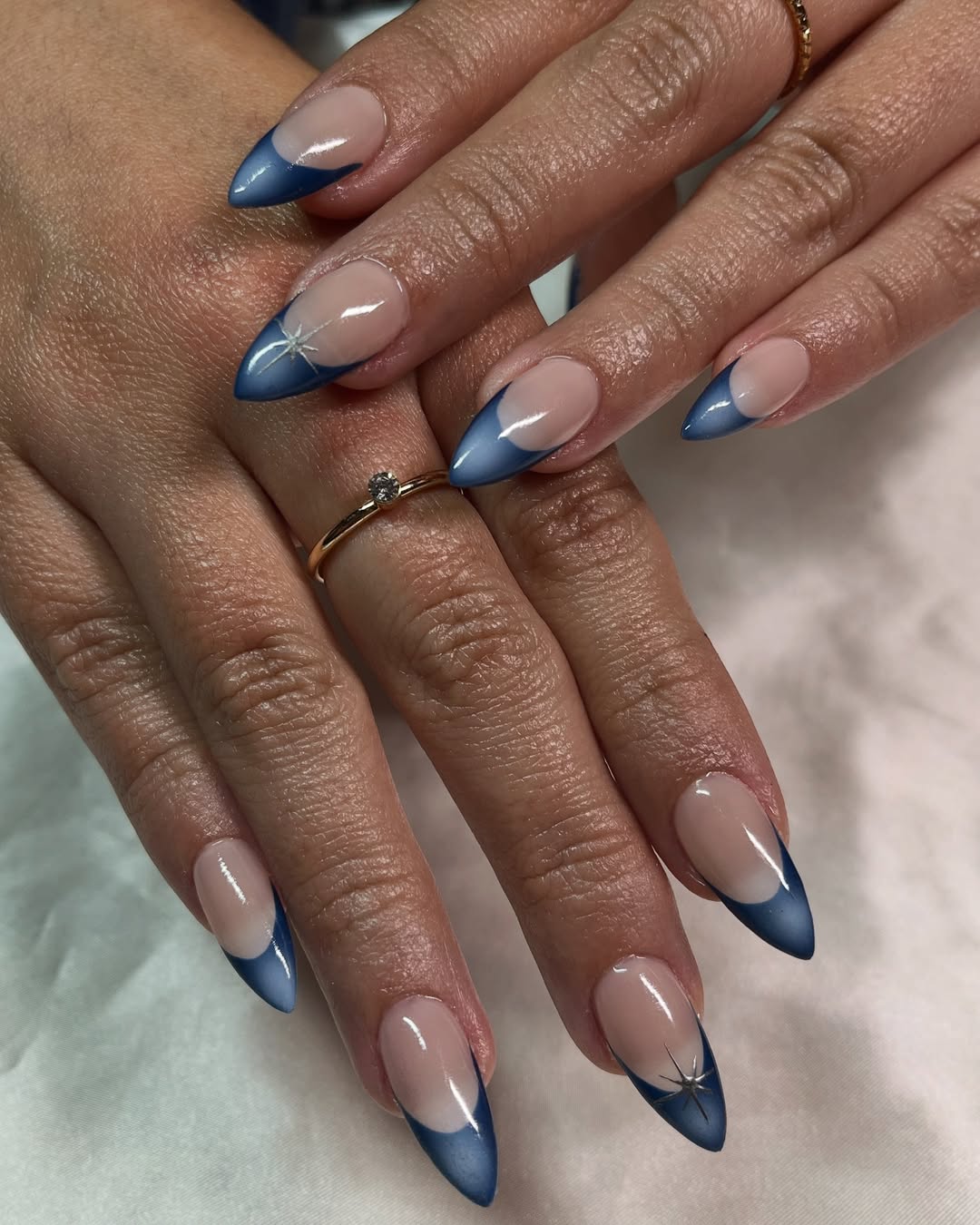 Almond nails with a nude base fading into midnight blue tips with subtle starburst accents on two nails