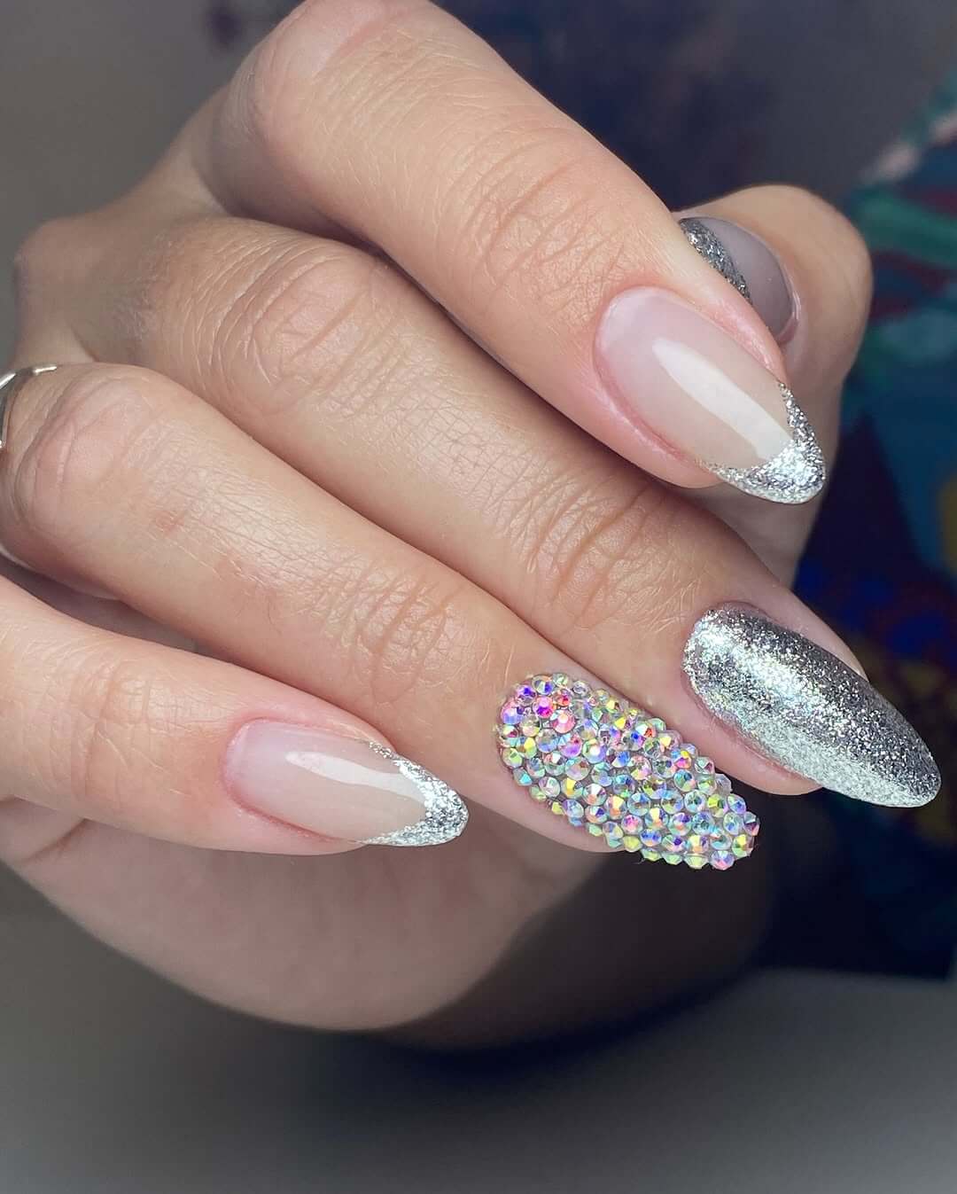 Nude almond nails with silver glitter French tips and crystal-covered accent nail