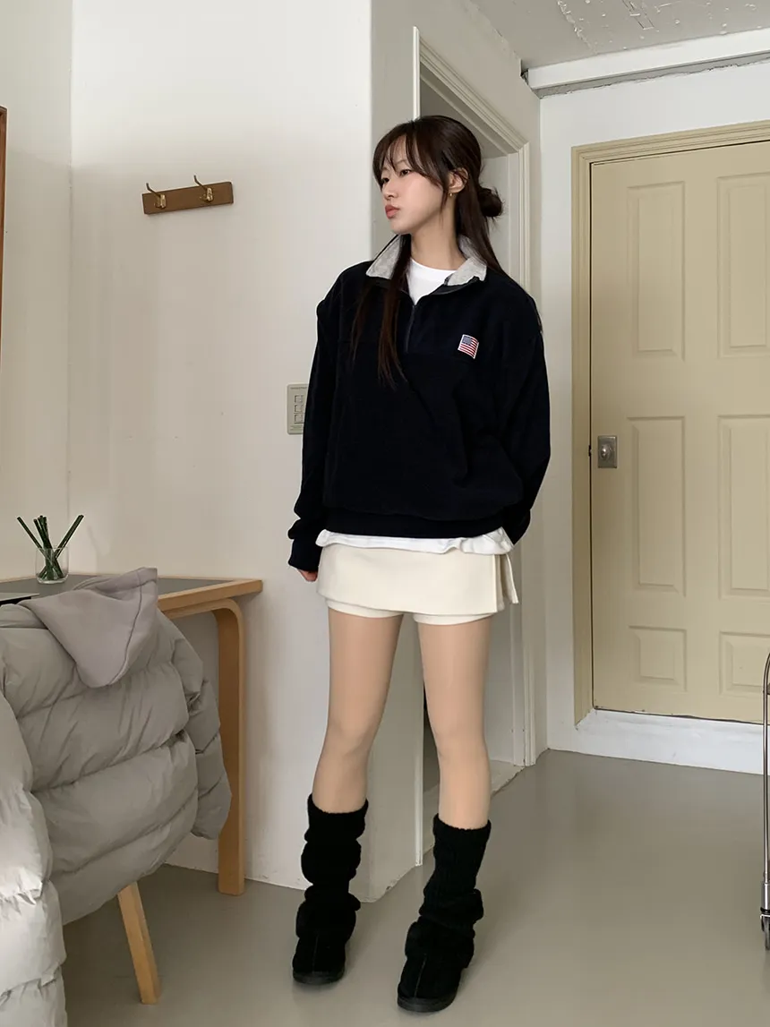 Woman in black quarter-zip fleece, white pleated mini skirt, sheer tights and black boots
