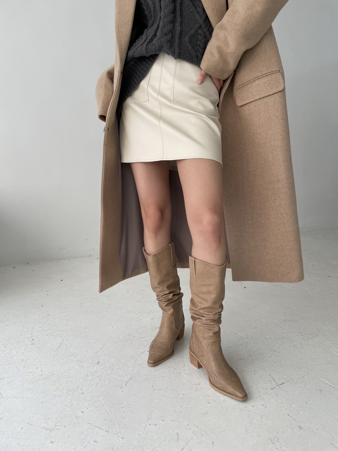 Cream knee-high boots with a cream leather mini skirt, dark knit and camel coat