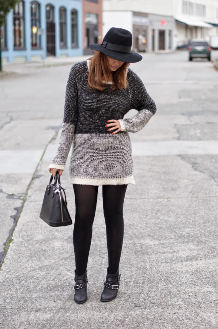 Woman wearing a grey marled sweater dress with black tights, ankle boots and a black fedora