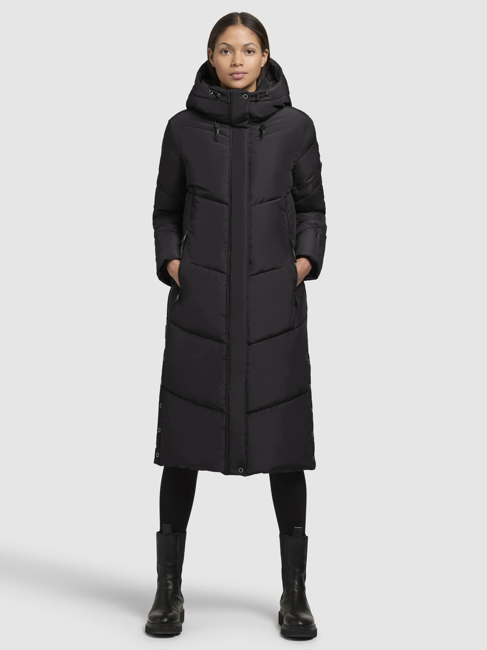 A black longline hooded puffer coat worn over black leggings with black mid-calf boots.