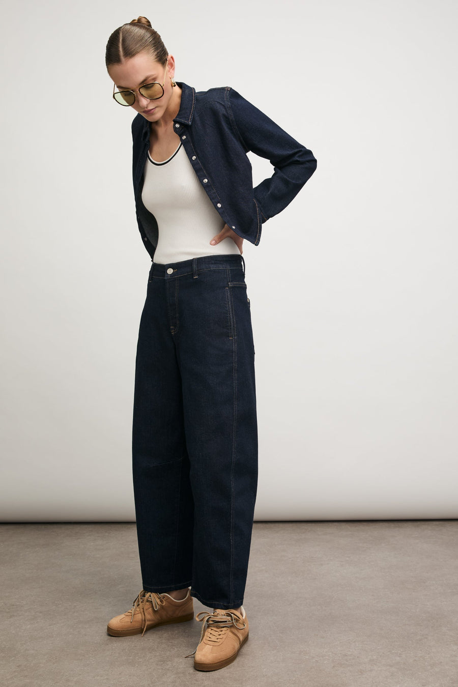 Model in a dark denim shirt and wide-leg jeans with tan sneakers