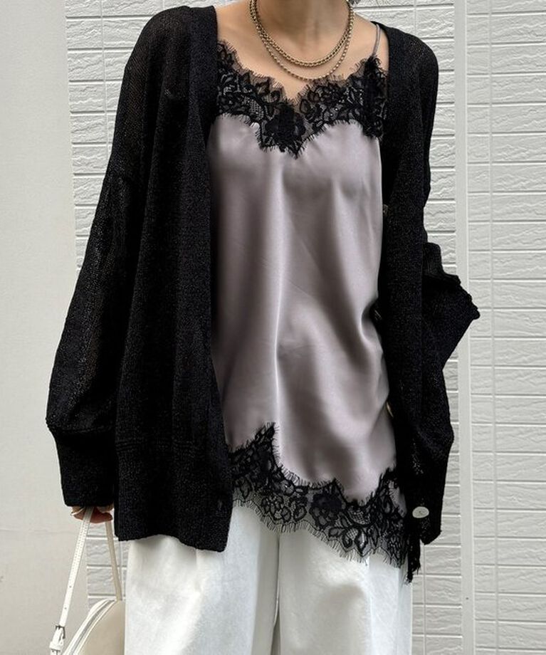 Woman wearing an open black knit cardigan over a champagne satin camisole with black lace trim and white wide-leg pants