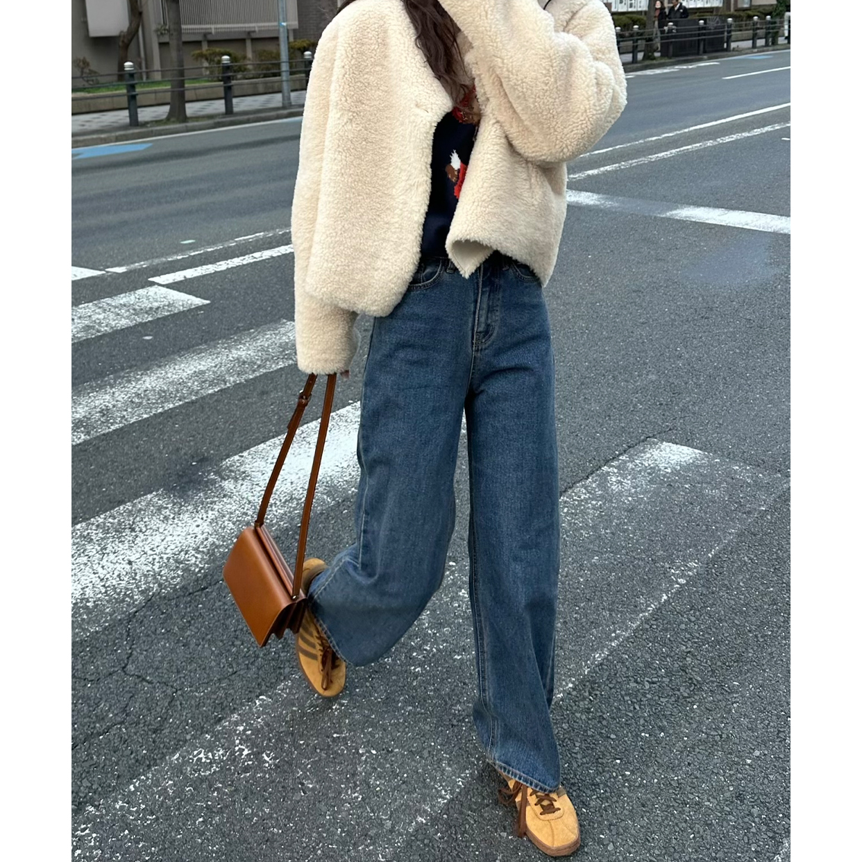 Person crossing the street in a cropped cream teddy jacket, wide-leg jeans and tan sneakers