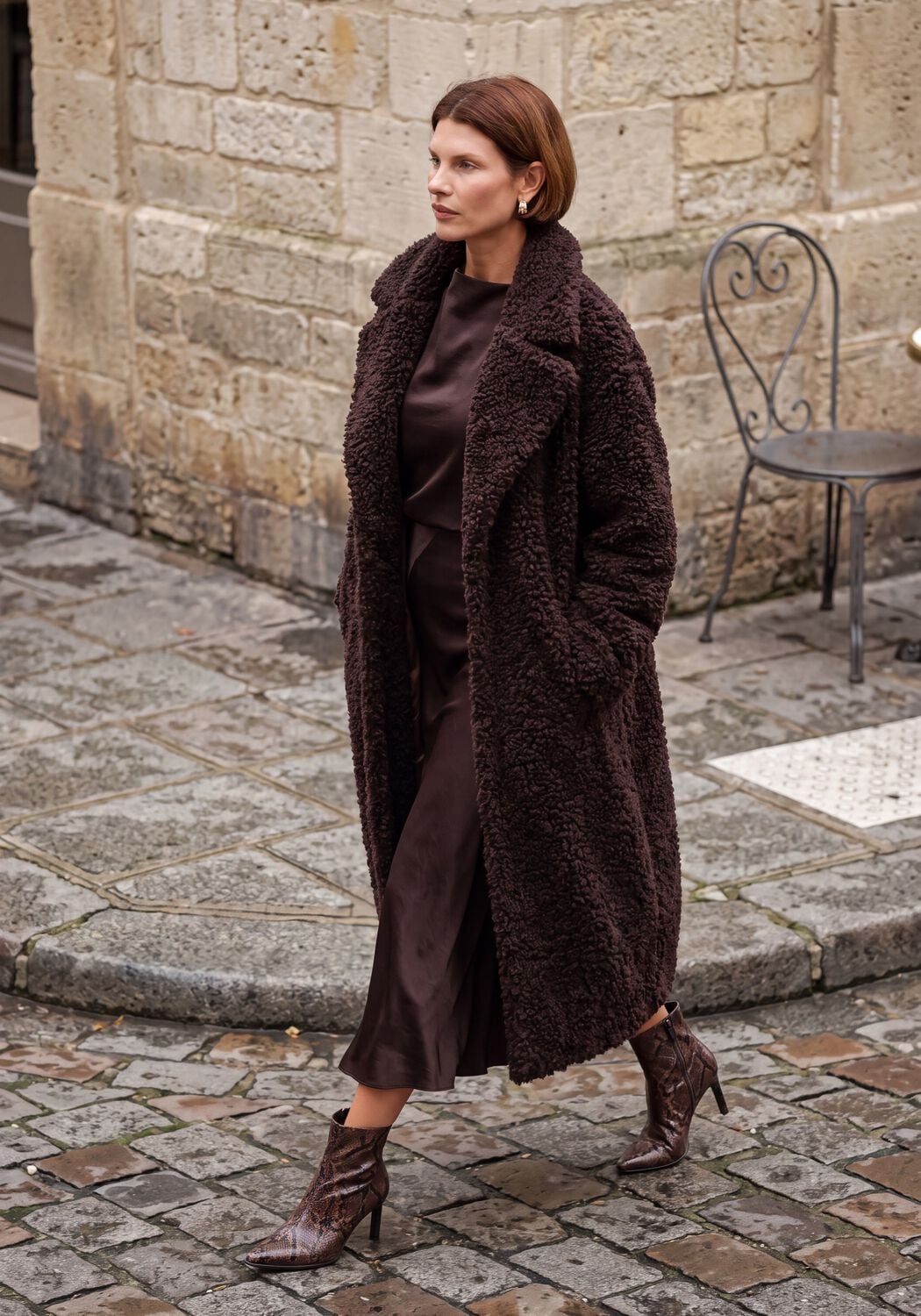 Woman in a chocolate teddy coat with a chocolate satin dress and snakeskin boots