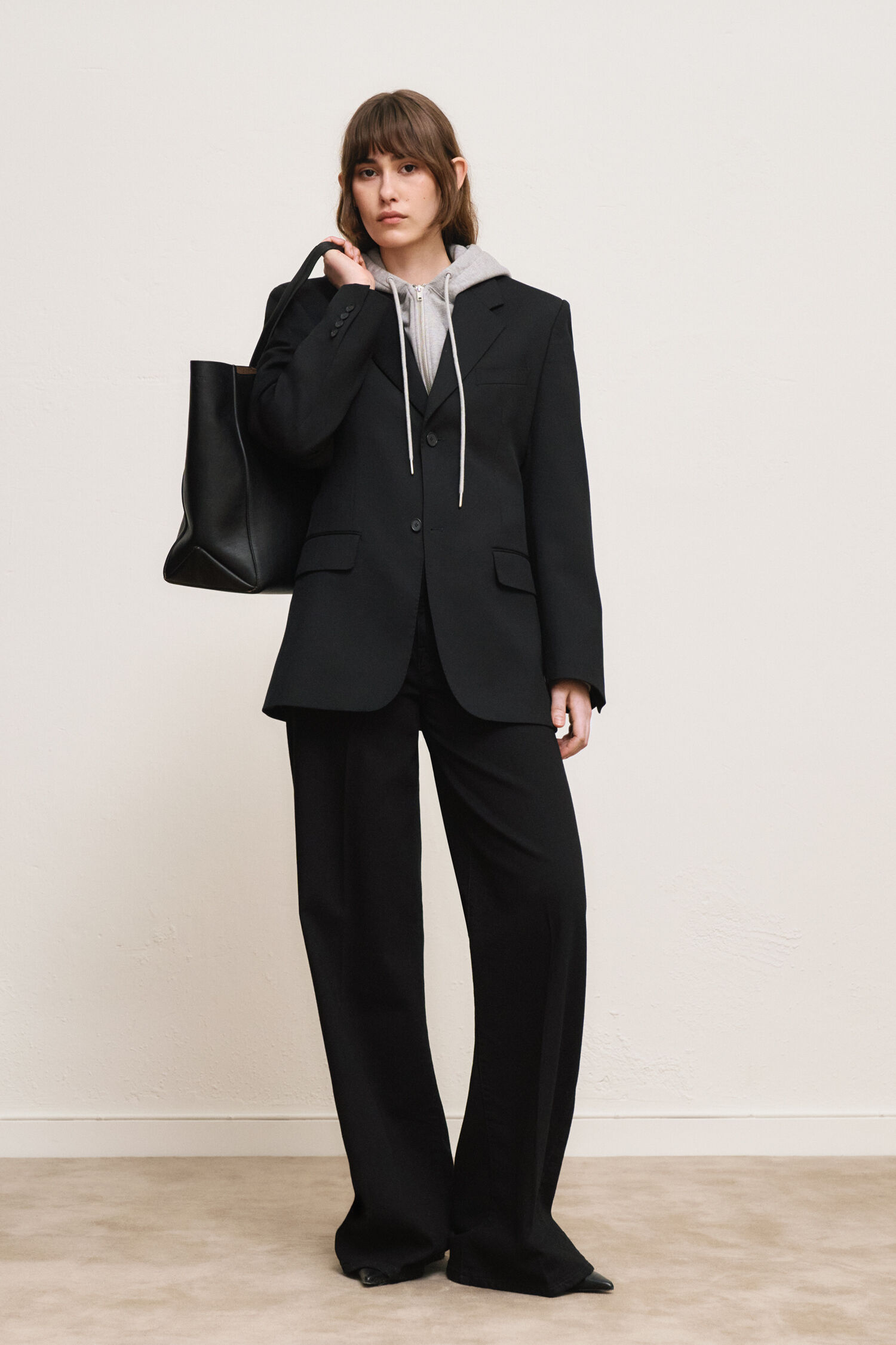 Woman in grey zip-up hoodie under black blazer with black wide-leg trousers