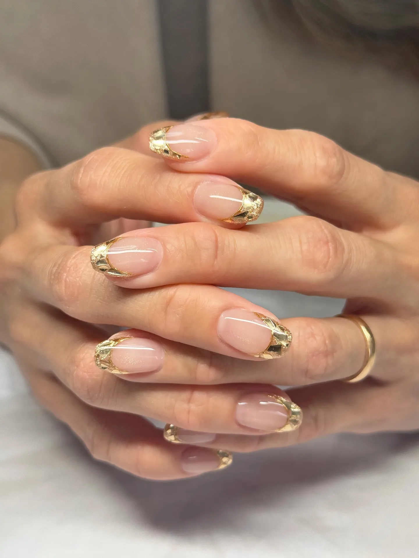 Almond nails with a sheer nude base and gold foil French tips