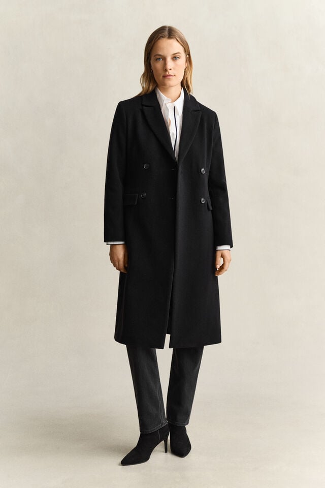 A black double-breasted long coat over a white shirt, dark jeans and black heeled boots.